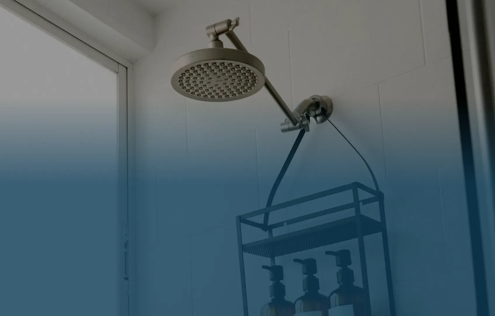 A modern bathroom with a metal showerhead and caddy holding bottles against white tiles. Soft lighting creates a calm and clean atmosphere.