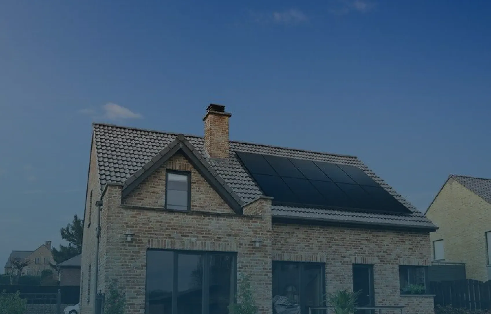 A modern brick house with a gray tiled roof features solar panels on top. The sky is clear and blue, conveying a sense of sustainability and tranquility.