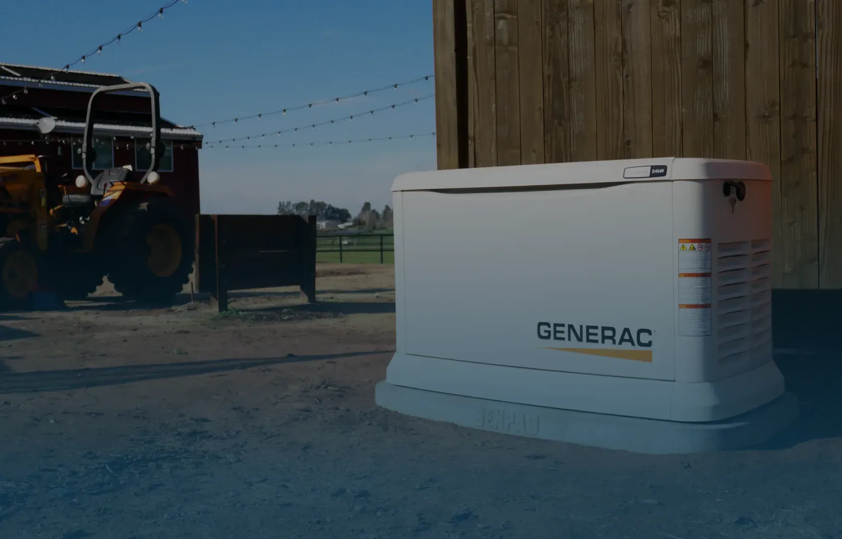 A white Generac generator sits on a gravel area beside a wooden building, with a tractor and string lights visible in the background, suggesting a rural setting.