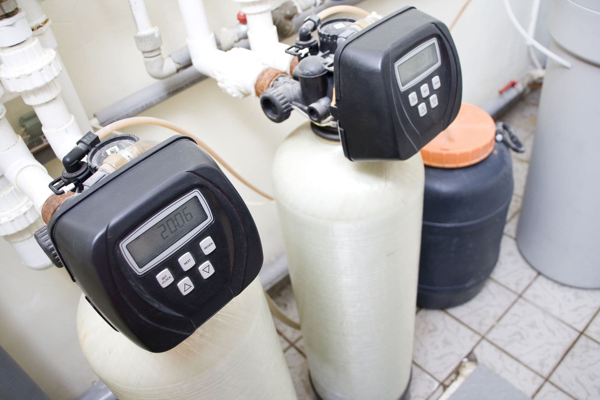 Industrial water filtration system with two digital control valves atop large tanks. Pipes and gauges surround the setup, indicating a utility room.
