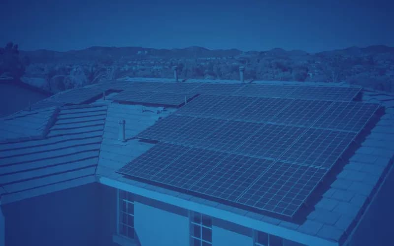 A rooftop is covered with solar panels under a blue tint, set against a background of distant hills and trees, conveying sustainability and innovation.