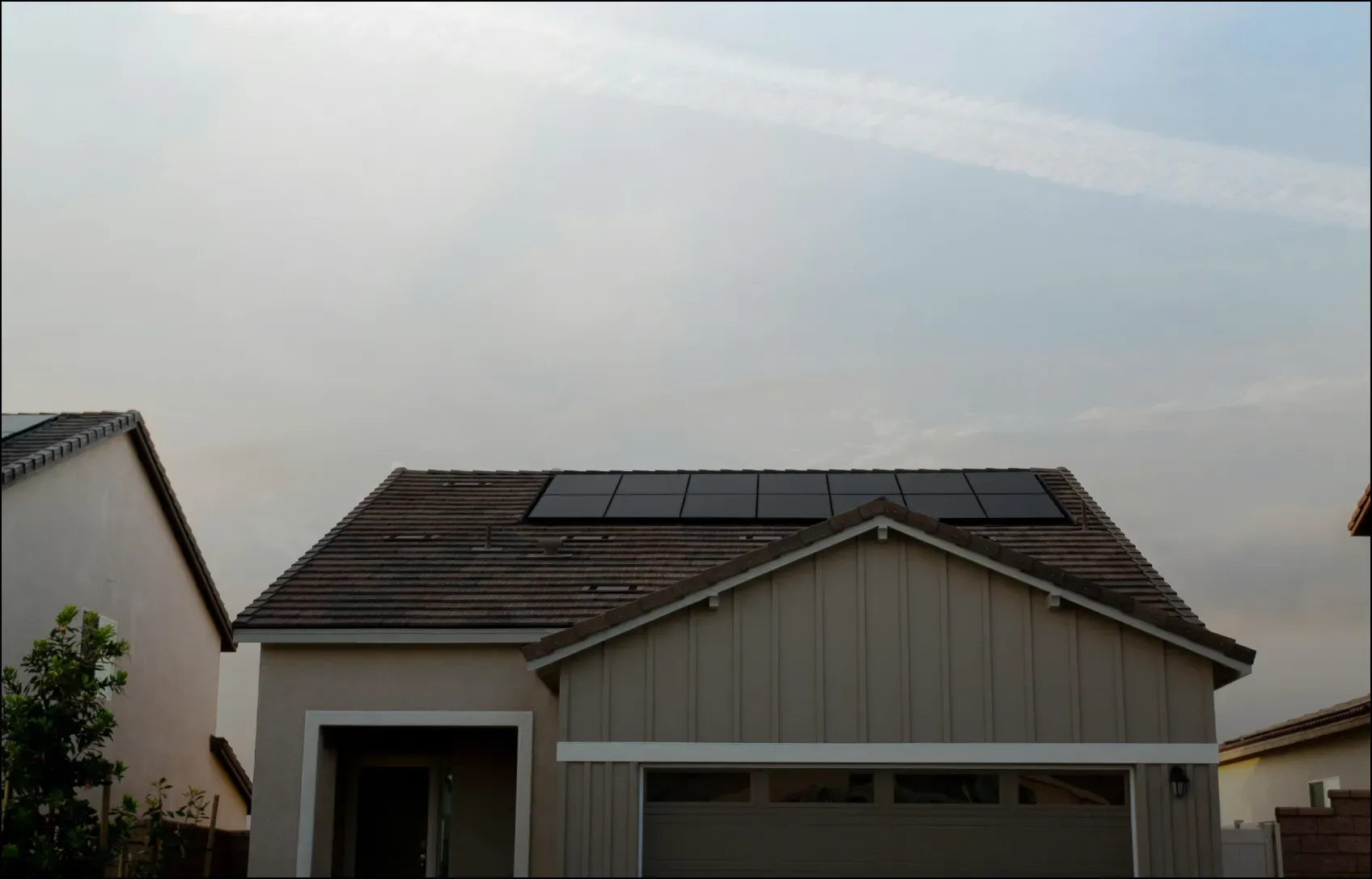 A modern, single-story house with solar panels installed on its roof under a cloudy sky, conveying a sense of sustainability and eco-friendliness.