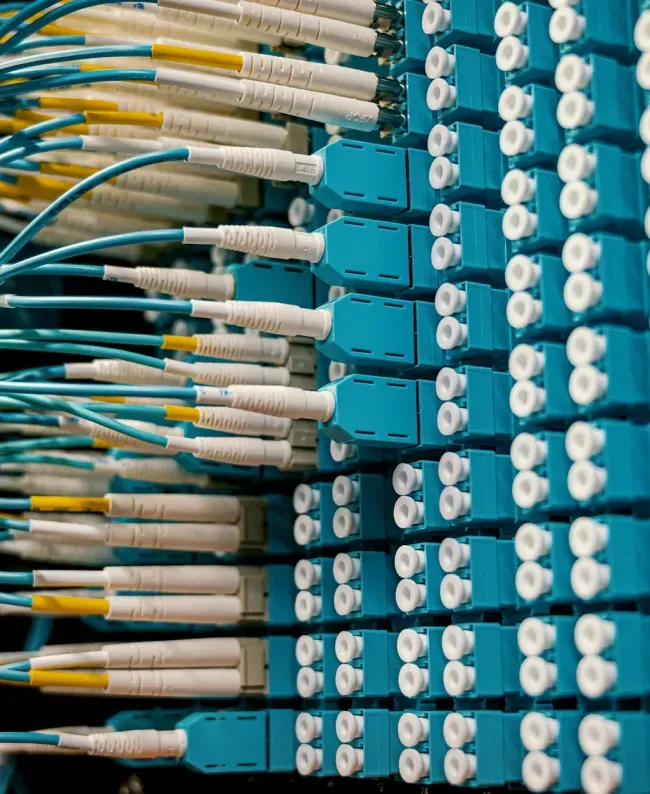 Close-up of a network server rack filled with turquoise and white fiber optic cables, conveying a sense of complex, high-tech connectivity.