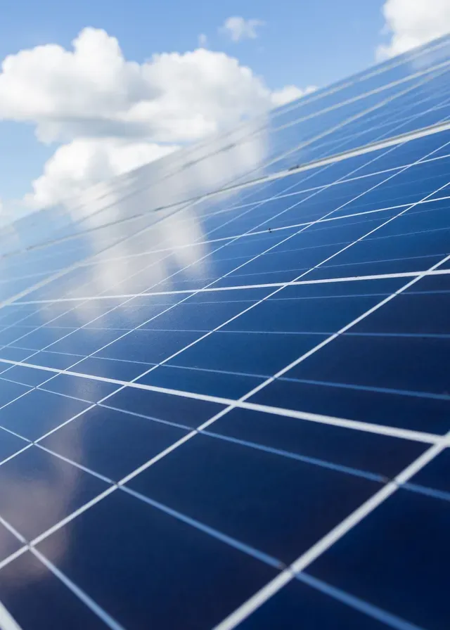 Close-up of a reflective solar panel under a bright blue sky with fluffy white clouds. The clean energy theme conveys a sense of sustainability.