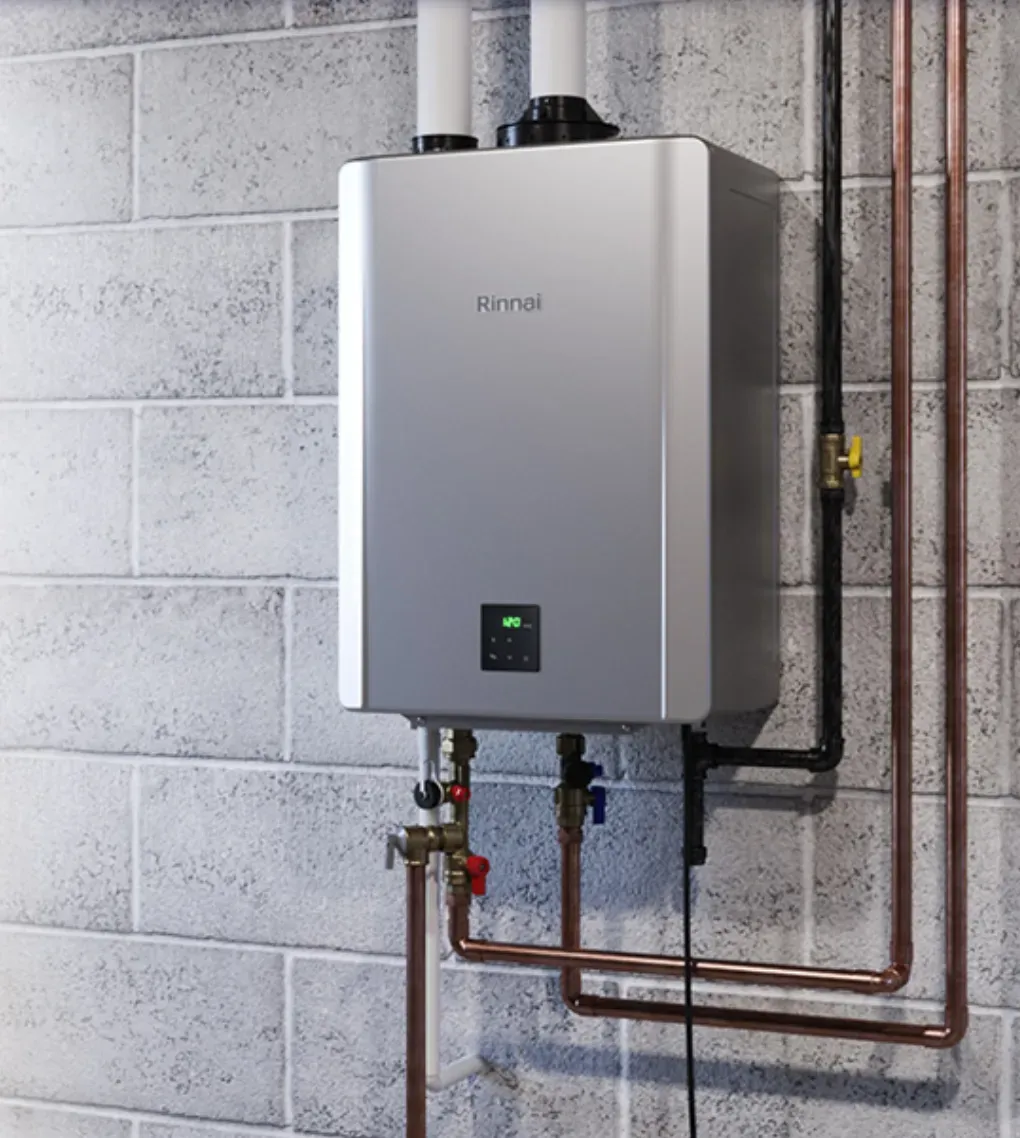 A sleek, modern tankless water heater mounted on a gray brick wall. Copper pipes connect underneath. The unit displays a digital temperature reading.