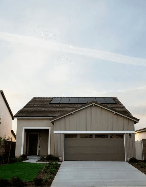 Modern suburban house with solar panels on the roof, a clean driveway, and a well-maintained lawn under a clear sky, conveying eco-friendly living.