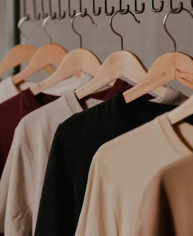 Neutral-toned t-shirts on wooden hangers. The shirts are arranged neatly, creating a calm and organized feel in a closet setting.