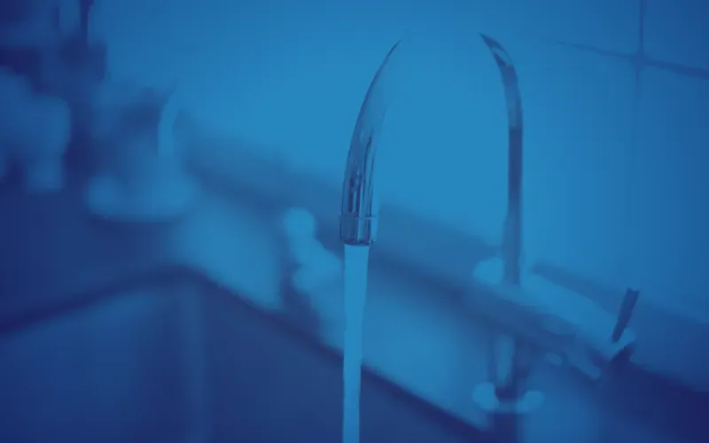A blurred photo with a blue tint shows water flowing from a modern kitchen faucet into a sink, evoking a calm and clean atmosphere.